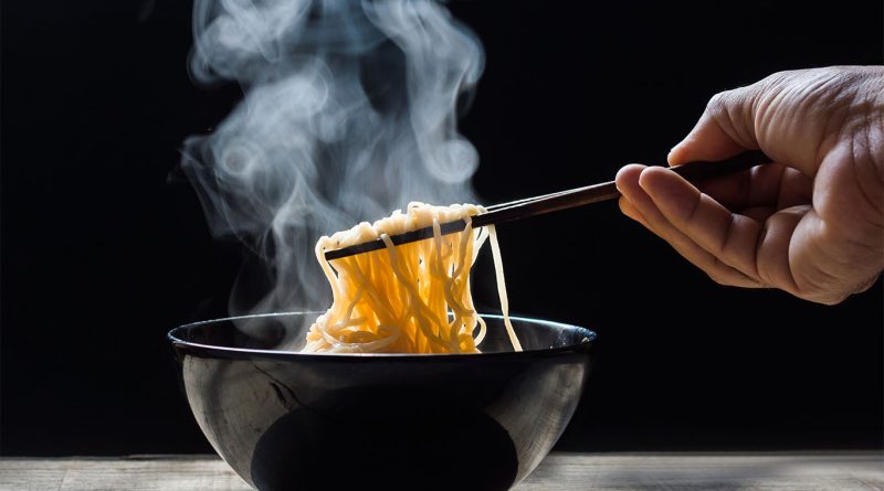 Image of a black bowl with noodles in and someone using chopsticks to pull them out to support indo chinese food article