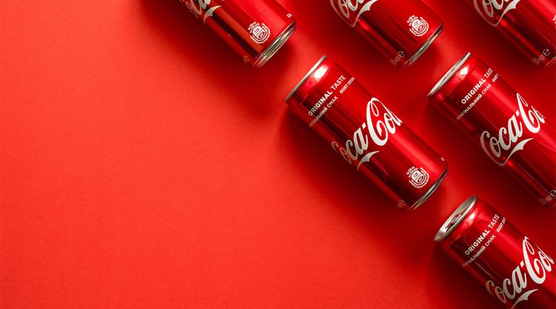 Image of multiple Coca Cola cans laid on a red background to support Coca Cola ad article