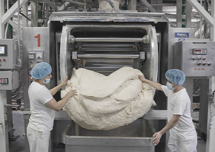 Two bakers taking a large amount of dough out of a machine