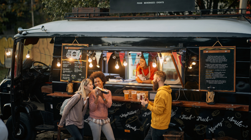 A group of people enjoying street food in front of a stylish black food truck.