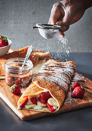 dusting a pancake wrap with icing sugar