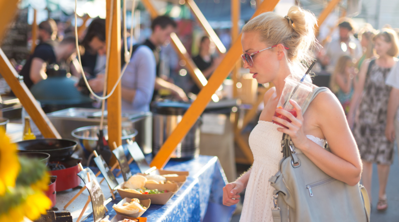 A woman enjoying a vibrant food festival, browsing artisanal food stalls with plant-based and local cuisine options, highlighting the 2024 food festival trends.