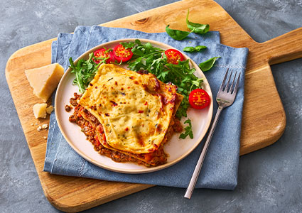 Plate of Lasagne on a blue napkin on a wooden chopping board