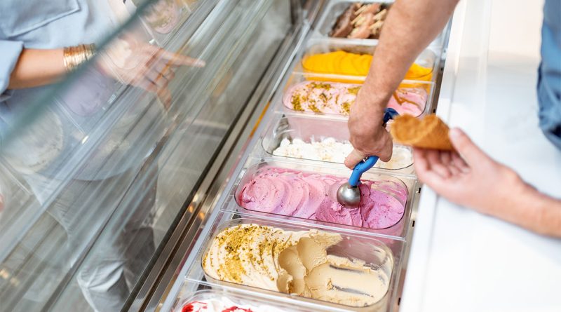 The End of Synthetic Colors in Ice Cream Signals a Bigger Food Shift A server scoops naturally colored ice cream into a cone at a display counter, showcasing a variety of pastel-toned flavors without artificial dyes.