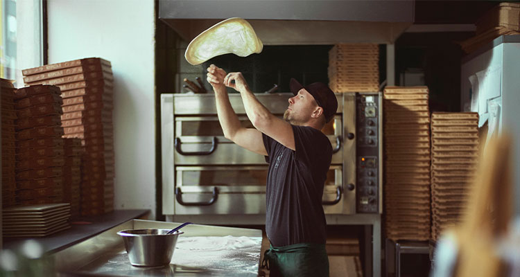 a person, skillfully tossing pizza dough in a kitchen setting