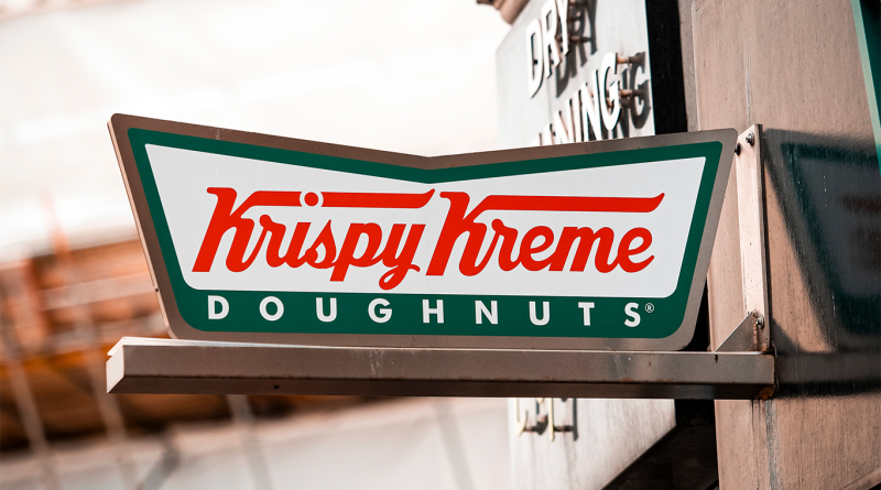 Krispy Kreme storefront sign mounted on a building exterior with the brand’s red and green logo prominently displayed.
