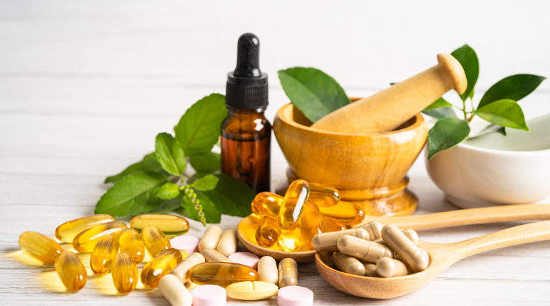 Dietary supplements, herbal capsules, and a dropper bottle arranged with fresh leaves and a wooden mortar and pestle.