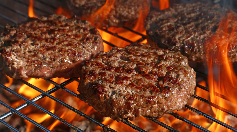 Close-up of beef burgers grilling over open flames on a barbecue grill.
