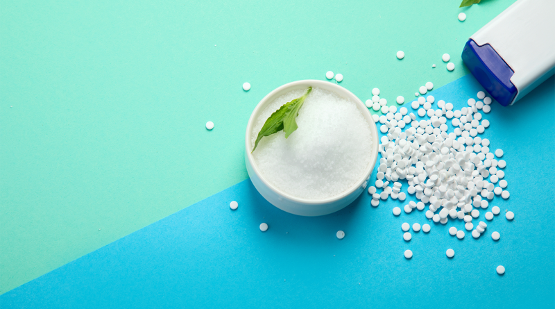 Bowl of granulated sweetener alongside white sweetener tablets on a blue and green background, illustrating sugar alternatives and low-calorie sweeteners used in food and beverage products.