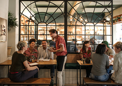 a lively indoor restaurant scene with customers seated at wooden tables, enjoying their meals