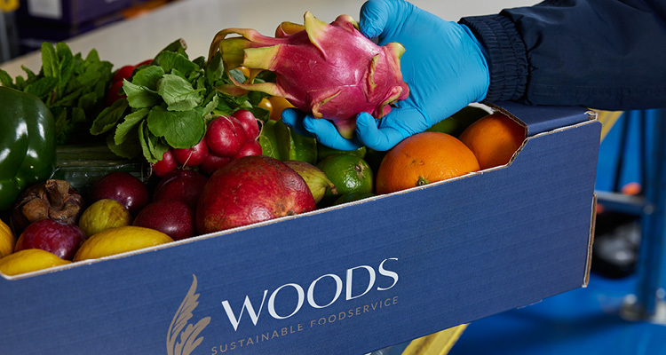 a person wearing a blue protective glove holding a vibrant pink dragon fruit over a blue woods Foodservice delivery box