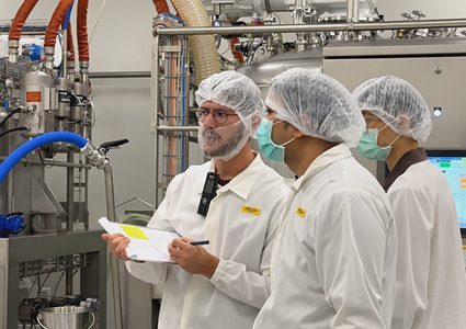 orkers in a factory setting wearing white coats and protective headgear