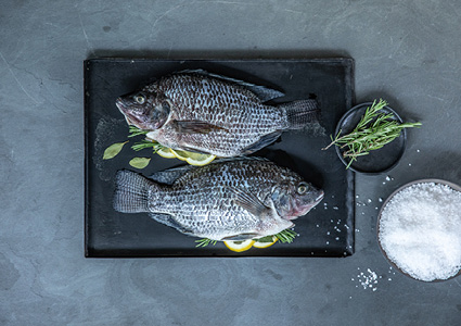 two whole sea bream fish arranged on a black serving board