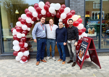 a Costa Coffee team celebrating a store opening with a large red and white balloon arch