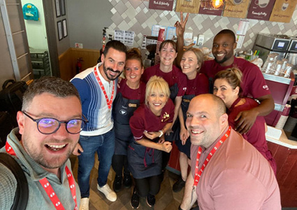 a group of workers wearing dark aprons over their clothes while smiling in a Costa Coffee store