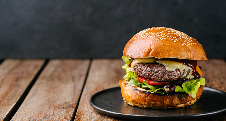 a gourmet cheeseburger served on a dark plate atop a rustic wooden surface