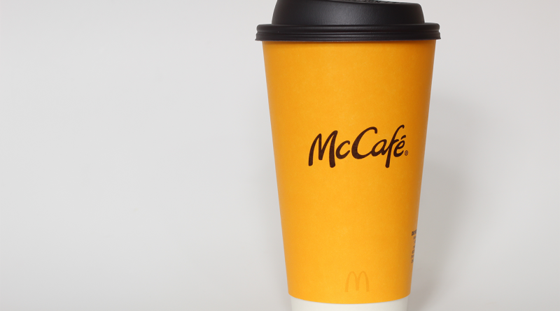 McCafé hot coffee in a yellow McDonald’s takeaway cup with a black lid.