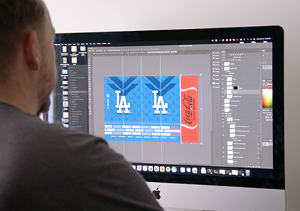 a designer working on an Apple desktop computer, using graphic design software to create a custom product label