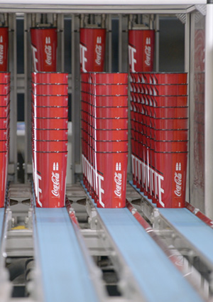 Stacks of red Coca-Cola branded aluminium beverage cans are organized in vertical rows moving along automated blue conveyor belts