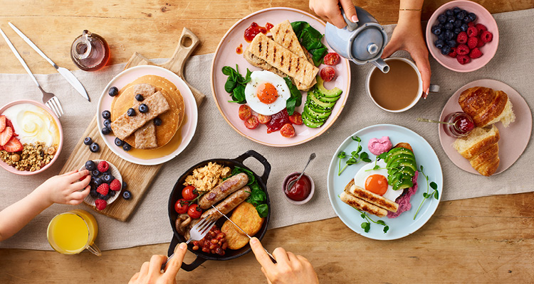 a top-down view of a full breakfast spread laid out on a light wooden table.