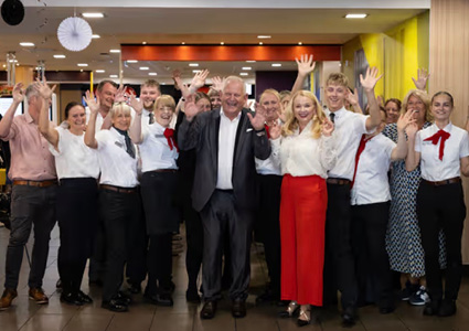 Eddie Leligdowicz, a prominent McDonald's franchisee who operates multiple restaurants, stands at the center of a cheerful team photograph alongside his wife, Maria