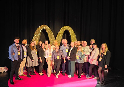 a group of people posing together on a stage in front of large, illuminated golden McDonald's arches