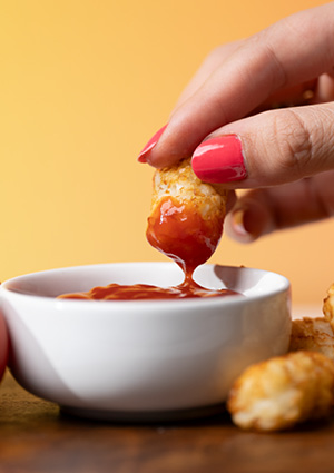 a crispy tater tot being dipped into a small white bowl of sauce
