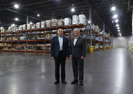 Two men stand side-by-side in the center of a spacious, modern warehouse