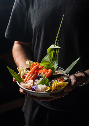 a person holding a ceramic bowl filled with an assortment of fresh Japanese sashimi