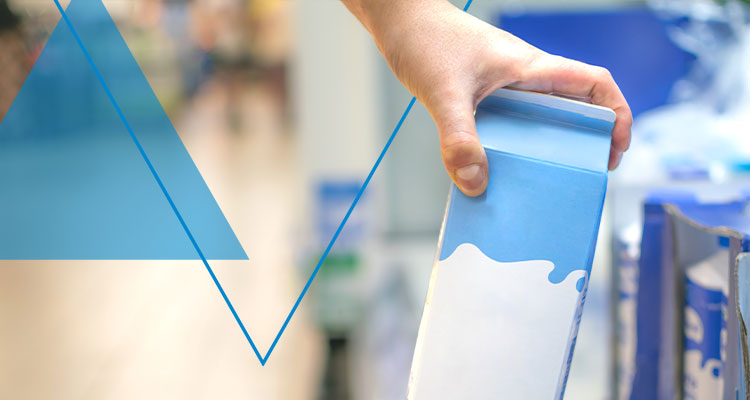 a hand holding a blue-and-white milk or beverage carton in a supermarket aisle