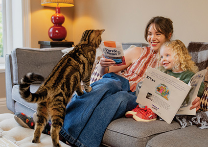 a tabby cat standing on a sofa next to a woman and a young child who are reading