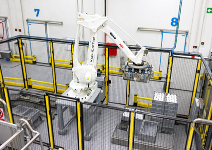 an industrial Xolertic Group robotic palletizer cell enclosed by yellow and black safety fencing